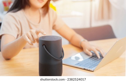 Young Asian woman listening to music by wireless portable speaker while working at home. Modern sound system.
