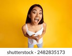 A young Asian woman with long dark hair is wearing a white tank top. She is smiling with her mouth open wide, looking directly at the camera, high angle view