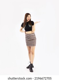 Young Asian Woman Long Hair In Black Crop T Shirt And Skirt With Ankle Boots Posing Standing And Pointing On White Background. Full Body Model.