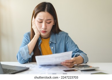 Young Asian woman looking at credit card invoice in her hands and worry about cash on bills payday