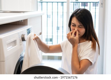 Young Asian Woman Looking At  Dirty Smelly Clothe Out Of Washing Machine In Kitchen.