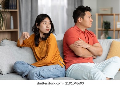 Young Asian Woman Looking At Her Angry Husband, Upset Chinese Couple Sitting On Couch Back To Back, Having Fight, Experiencing Difficulties In Relationships, Home Interior, Copy Space