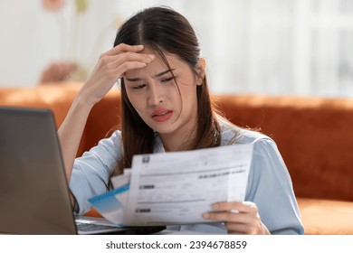 Young Asian woman looks stressed while examining a bill, impactful financial pressure, anxiety, and the challenges of managing expenses. Financial problem. - Shutterstock ID 2394678859