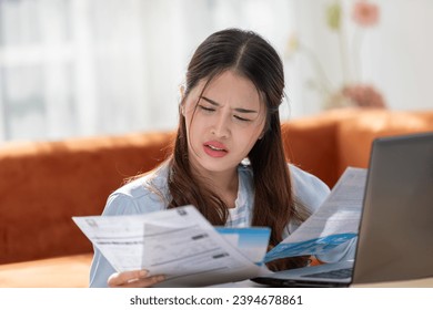 Young Asian woman looks stressed while examining a bill, impactful financial pressure, anxiety, and the challenges of managing expenses. Financial problem. - Shutterstock ID 2394678861