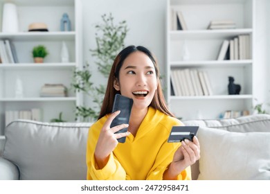 Young asian woman lying on sofa in living room, makes online banking payments through the internet from bank card on cell phone. Shopping online on mobile with credit card - Powered by Shutterstock