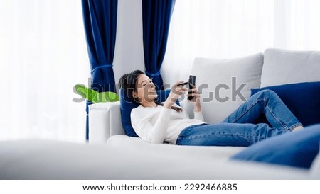 Young asian woman lying on sofa in living room, makes online banking payments through the internet from bank card on smartphone. Shopping online on mobile phone with credit card