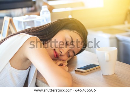Young Asian Woman lying in wait for someone, There is a telephone and a white coffee cup beside it  in coffee shop.