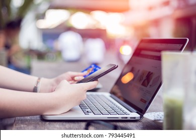 Young asian woman making payment on mobile smart phone and credit card for shopping on online retail shop with laptop computer at coffee cafe, lifestyles technology