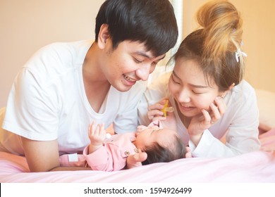 Young Asian Woman And Man Playing With A Newborn Baby On The Bed. Happiness And Family Concept