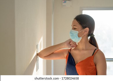 Young Asian Woman With Mask For Protection From Corona Virus Outbreak Pressing Elevator Door With Elbow To Avoid Infection