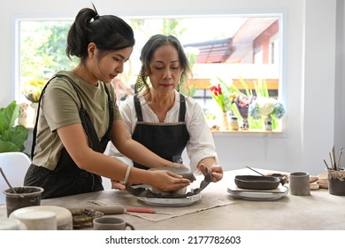 Young Asian Woman And Mature Woman Enjoy Making Ceramics In Pottery Workshop. Activity, Handicraft, Hobbies Concept