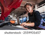 Young asian woman mechanic using a laptop while working on a car engine in a repair shop, showcasing expertise and modern technology in automotive maintenance