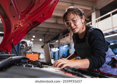 Young asian woman mechanic using a laptop while working on a car engine in a repair shop, showcasing expertise and modern technology in automotive maintenance - Powered by Shutterstock