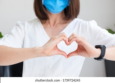 Young Asian Woman With A Medical Mask On Face Makes A Heart Out Of Her Hands. The Concept Of Thanks To Health Workers To Cheer And Love