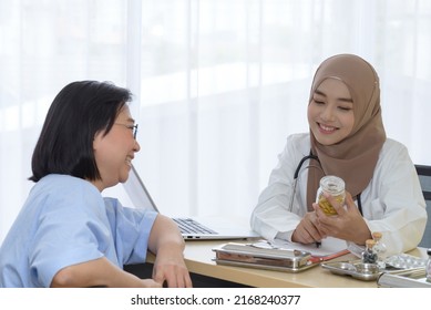 Young Asian Woman Muslim Doctor Holding The Bottle Of Pills And Explaining To Elderly Patient In The Hospital Office