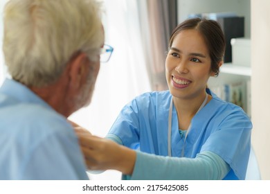 Young Asian woman nurse helping get dress to disabled elderly man in bed at retirement home. Millennial caregiver assisting handicapped senior patient, taking care of older male indoors