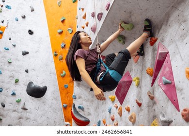 A young Asian woman on a climbing wall. A Korean girl climbs a bouldering wall. Attractive professional sport climber woman having training in the gym. Charming brunette having active time. - Powered by Shutterstock