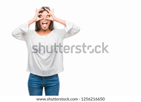 Young asian woman over isolated background doing ok gesture like binoculars sticking tongue out, eyes looking through fingers. Crazy expression.