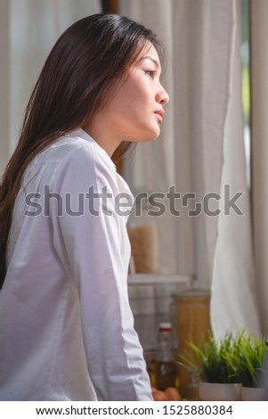 Young Asian woman in panties and long shirt rested in the kitchen at home and looked out the window