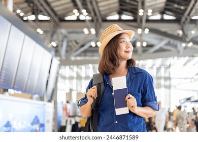 Young Asian woman passenger with carry on luggage is looking at her boarding pass after self check kiosk in at airport terminal for international travel flight and vacation - Powered by Shutterstock