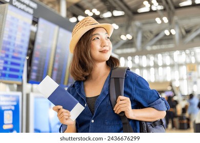 Young Asian woman passenger with her carry on luggage is looking at her boarding pass after self check kiosk in at airport terminal for international travel flight and vacation  - Powered by Shutterstock