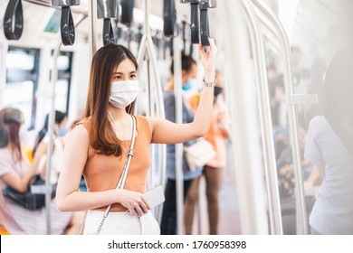 Young Asian woman passenger wearing surgical mask and listening music via smart mobile phone in subway train when traveling in big city at Covid19 outbreak, Infection and Pandemic concept