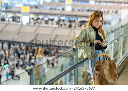 Young Asian woman passengers with suitcase using mobile phone booking hotel during waiting flight at boarding gate in airport terminal. Attractive girl tourist travel by airplane on holiday vacation