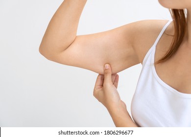 Young Asian woman pinching loose skin or flab on her upper armon white background. Health care and medical concept