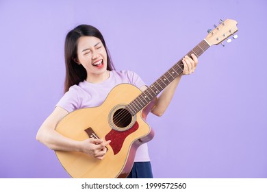 Young Asian Woman Playing Guitar On Purple Background