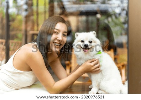 Young Asian woman playing with her pomeranian dog at pet friendly cafe. Domestic dog with owner have fun outdoor lifestyle travel city on summer vacation. Pet Humanization or pet parents concept.