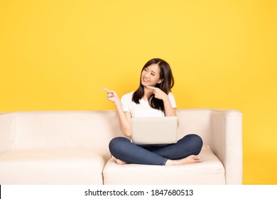 Young Asian Woman Point Finger On Comfortable Couch, Using Laptop At Home, She Is Happy To Spend Some Free Time Online While Chatting With Friends In Social Network, Shopping Or Working Online.