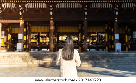 Young Asian woman praying in traditional Meiji Jingu Shrine in Tokyo city, Japan. Attractive girl tourist travel Japan landmark famous place and learning Japanese culture in autumn holiday vacation.