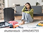 young Asian woman Preparing suitcase for summer vacation trip. Young woman checking accessories and stuff in luggage on the sofa at home before travel.