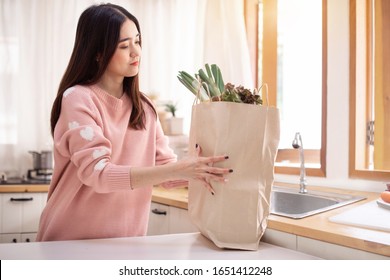 Young Asian Woman Puts A Grocery Shopping Bag On Table In Her  Kitchen 