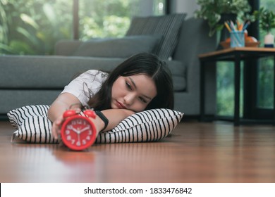 Young Asian Woman Reaching Over To Turning Off Alarm Clock While Lying On The Floor In Living Room At Home.