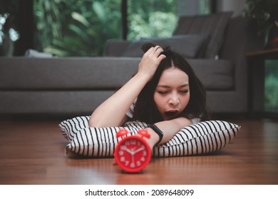 Young Asian Woman Reaching Over To Turning Off Alarm Clock While Lying On The Floor In Living Room At Home.