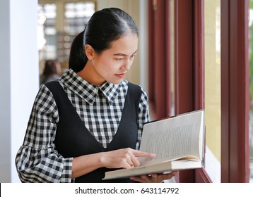 Young Asian Woman Reading Book In The Library.