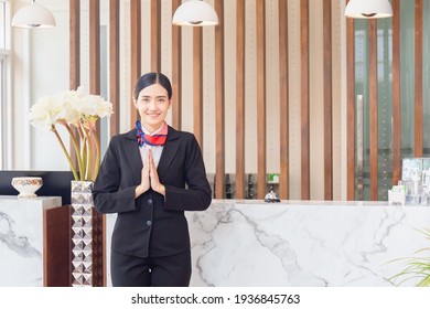 Young Asian Woman Receptionist At Reception Desk With Pay Respect. Portrait Of Smiling Female Receptionist Working In Hotel