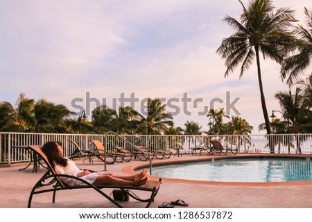 Young asian woman reclines back on a sunbed next to a swimming pool. Vacation concept in Hawaii