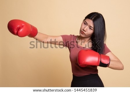 Young Asian woman with red boxing gloves on beige background
