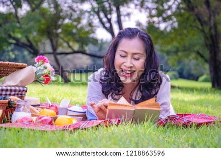Young Asian woman relax time in park.In the morning she is reading book , smile and  laugh .She is  lying on the grass beside picnic basket. 