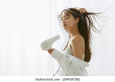 A young Asian woman relaxing with a hair dryer