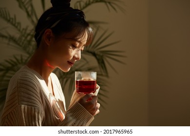 A young Asian woman relaxing at home drinking fruit tea