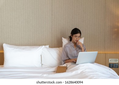 Young Asian Woman Relaxing In The Hotel And Working With Laptop On A Bed, Business Trip, Working Travel Concept