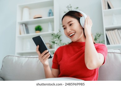 Young Asian woman relaxing on sofa at home, listening music with headset on cell phone. People lifestyle concept - Powered by Shutterstock