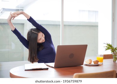 Young asian woman is relaxing to stretching and eating bread with a glass of orange juice while break time after working hard at home