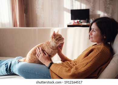Young Asian Woman Resting With Pet In Sofa At Home In Sunny. Beautiful Ginger Tabby Cat. Animals And Lifestyle Concept.