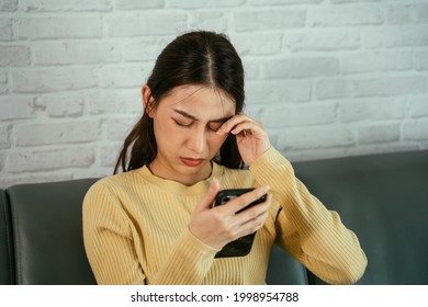 Young Asian Woman Rubbing Eyes Due To Feeling Of Discomfort From Using Smartphone For Long Hours Without Rest And Break At Home