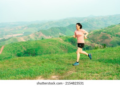 Young Asian Woman Runner, Wearing Black Sportswear, Running On A Big Mountain Trail, Cool Morning, Windmills, And Sky In The Background.