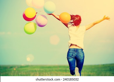 Young asian woman running and jumping on green grassland with colored balloons 